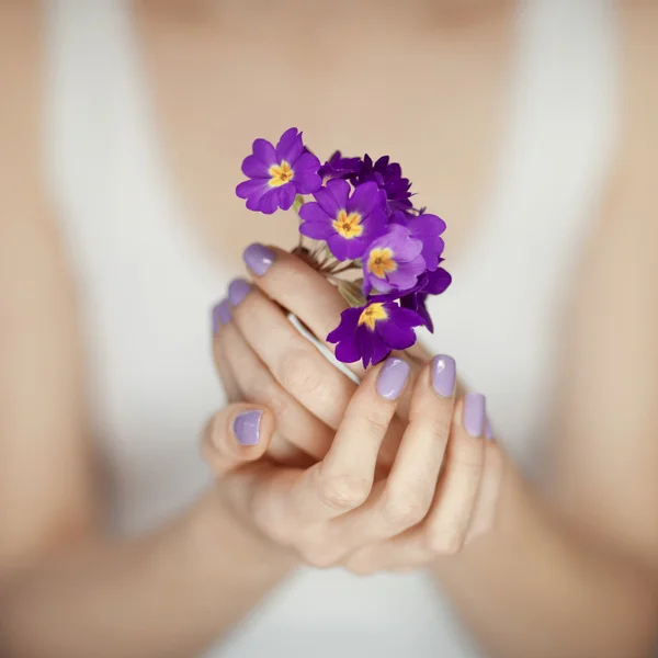 Mãos de mulher com belas unhas em roxo segurando flores — Fotografia de Stock