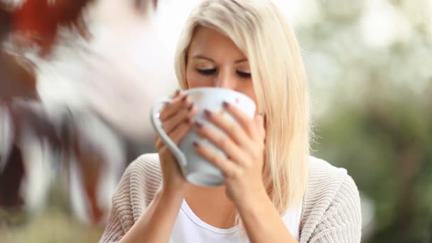 Schöne, blonde junge Frau trinkt Tee im Garten — Stockvideo