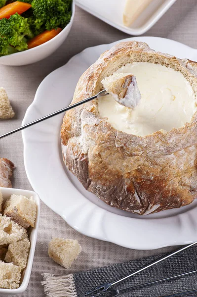 Creamy cheese fondue inside Italian bread. Fork dipping bread in cream cheese