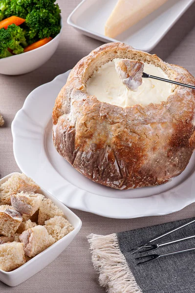 Creamy cheese fondue inside Italian bread. Fork dipping bread in cream cheese