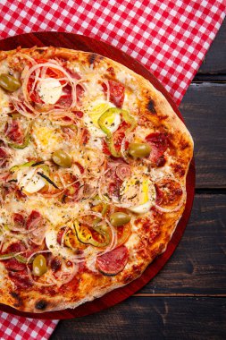 Sanatsal Brezilya pizzası, yukarıdan manzara. Dolmalık biber, soğan, pepperoni ve mozzarella ile. Ahşap bir temeli olan