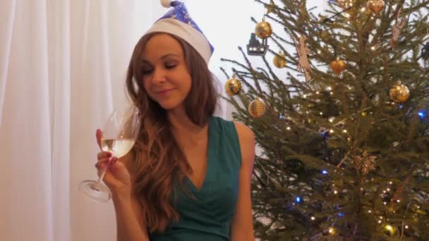 Egy hölgy vicces karácsonyi kalapban pezsgőt iszik mosolyogva. — Stock videók