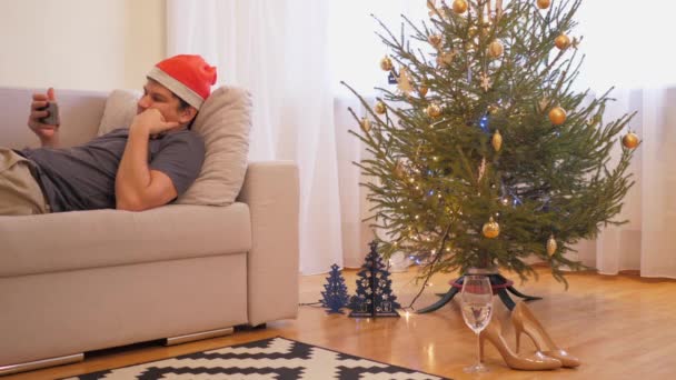 深刻な男で赤いクリスマスの帽子は退屈なニュースを見る — ストック動画
