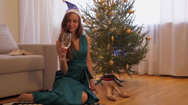 Slim woman sits with flute on floor against Christmas tree — Stock Video