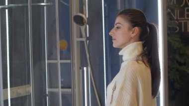 Uzun saçlı, at kuyruklu genç bir kadın duş kabinine bakıyor.