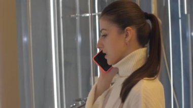 Üzgün yüzlü genç bir kadın, akıllı telefondan kocasıyla konuşuyor.