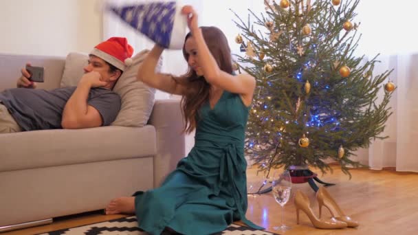 Barefoot woman puts on hat against Christmas tree and lights — Stock Video