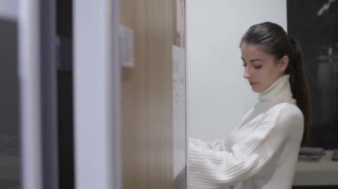 Atkuyruklu genç bir kadın kahverengi tahta kapıya yaklaşıyor.