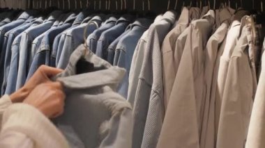 Genç kadın elleri siyah askıya gri gömlek giydirip asıyor.