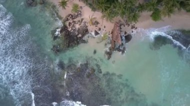 Beyaz köpüklü dalgalar kumlu sahilde okyanus suyunda yuvarlanıyor.