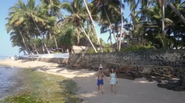 Çocuklu çift okyanus kıyısındaki kumlu sahil boyunca geziniyor.