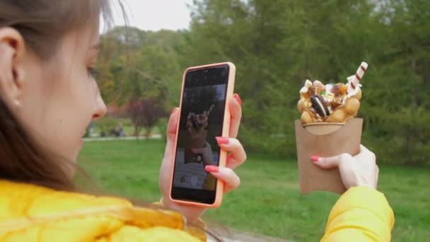 Kobieta robi zdjęcie smacznego koreańskiego wafelka w jesiennym parku — Wideo stockowe