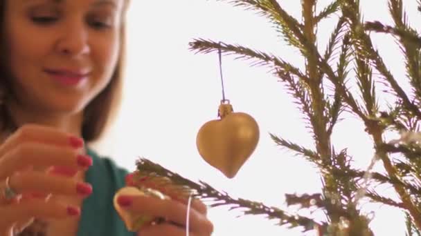 Μια χαμογελαστή γυναίκα κοιτάζει ένα παιχνίδι σε σχήμα καρδιάς κρεμασμένο στο έλατο — Αρχείο Βίντεο