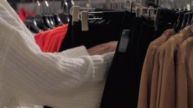 Genç kadın elleri kıyafetlerin arasında siyah elbiseler taşıyor.