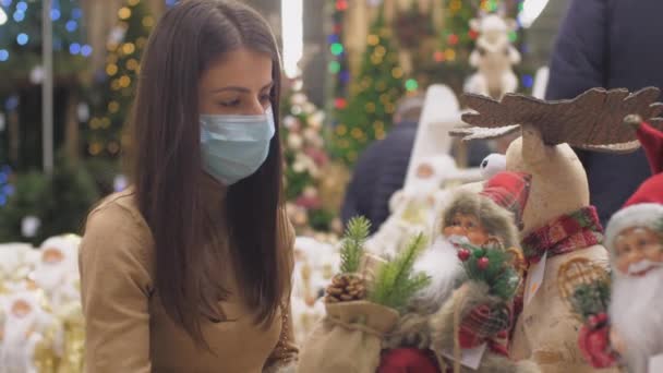 Yüz maskeli esmer, Noel Baba 'nın çantalı heykelciğine bakıyor. — Stok video
