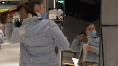 Alış veriş yapan kişi uzun saçlarını at kuyruğu yapıp mavi kot ceket dener.