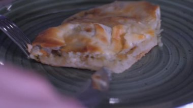 Gümüş çatal ve bıçak tutan kişi pizza dilimi kesiyor.