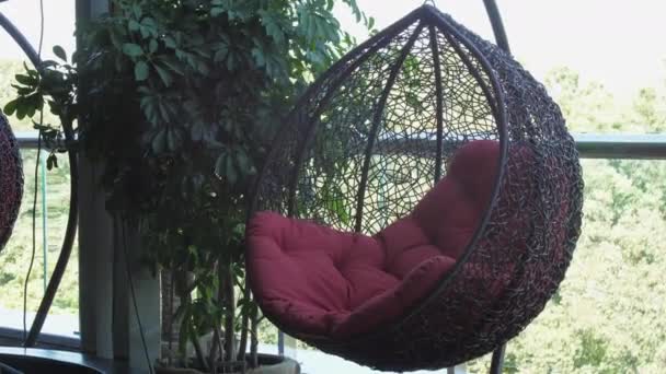 Fotel kokonowy z czerwoną poduszką wiszący na tarasie kawiarni — Wideo stockowe