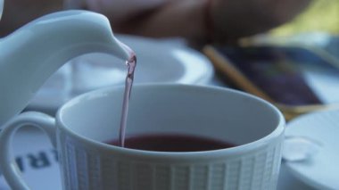 Beyaz seramik çaydanlıktan küçük fincanlara dökülen lezzetli çay.