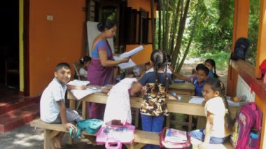 İlkokul öğretmeni çocuklara kağıt not defteri verir.