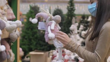 Yüz maskeli genç kadın komik, yumuşak bir geyik oyuncağı tutuyor