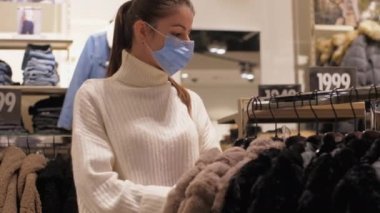 Yüzü maskeli sıska bayan kahverengi kışlık palto giyiyor.