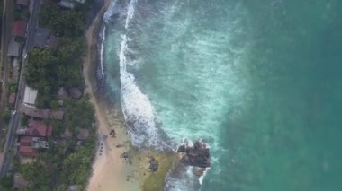 Beyaz köpüklü okyanus dalgaları sarı kumsalda yuvarlanıyor.