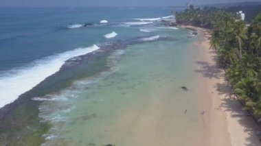 Beyaz köpüklü şeffaf okyanus dalgaları sarı kumda yuvarlanıyor.