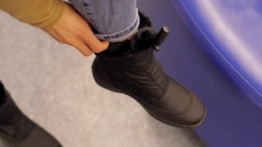 Kot pantolonlu kadın alışveriş merkezinde siyah kış ayakkabısı giyiyor.