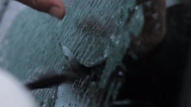 Kişi elektrikli araba camını plastik buz kazıyıcı ile temizliyor.