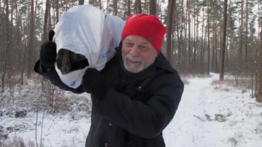 Gülümseyen sakallı oduncu karlı orman yolunda yürüyor.