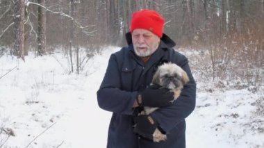 Sakallı emekli, karlı yolda köpek tutarak yürüyor.