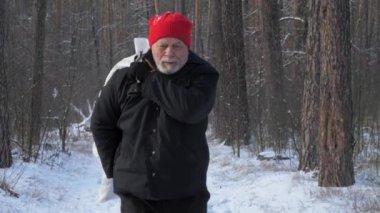 Sakallı emekli, elinde çantayla orman yolunda yürüyor.