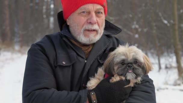Bearded pensioner walks along snowy road holding dog — Stock Video