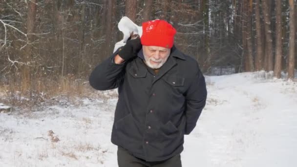 Wiek mężczyzna chodzi po śnieżnej drodze trzymając topór i torbę — Wideo stockowe