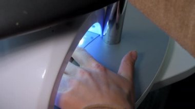 Güzellik salonu ziyaretçisi ultraviyole lambayla temel jeli kurutuyor.