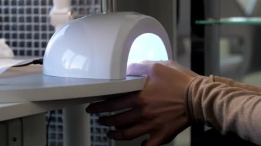 Modaya uygun bir kadın, tırnaklarını lamba kafesinde kurutuyor.