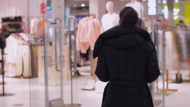 Dlouhosrstá brunetka v černém zimním kabátě procházky podél obchodu
