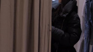 Tek kullanımlık maskeli genç bir kadın soyunma odasında duruyor.