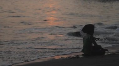 Kısa saçlı küçük kız dalgaların arasında oturuyor.