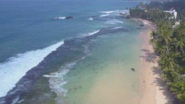 Beyaz köpüklü şeffaf okyanus dalgaları sarı kumda yuvarlanıyor.