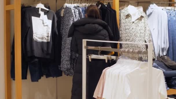 Jovem mulher na máscara facial caminha perto de ampla gama de roupas — Vídeo de Stock