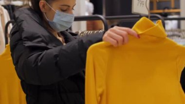 Tek kullanımlık maskeli genç kadın sarı kazak tutuyor.