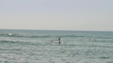 Sporcular büyük gök mavisi deniz yüzeyinde sörf yapıyor.