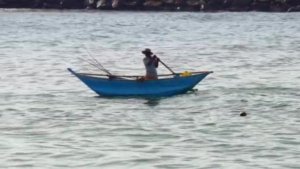 Человек плывет в голубой лодке, а серфер плывет вдоль океана. — стоковое видео