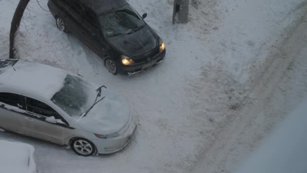 Černý automobil jezdí z parkoviště přes sníh — Stock video