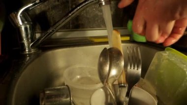 Kişi çatal bıçak takımını süngerle yıkayıp konteynıra koyar.