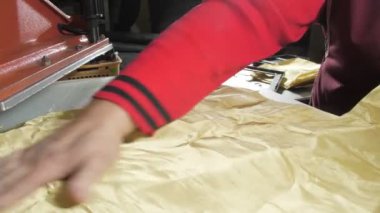 Atölye terzisi tezgahtaki sarı metal kumaşı düzleştirdi