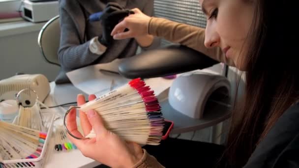 Long haired brunette looks at coloured examples of manicure — Stock Video