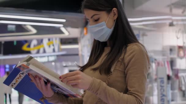 Jeune femme masquée tourne des pages de livre près des étagères — Video